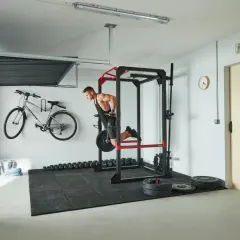 Mężczyzna wykonuje ćwiczenia na środek klatki piersiowej na drążku. W tle rower, hantle i sprzęt do treningu siłowego.