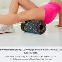Kobieta wykonuje rolowanie mięśni ud za pomocą czarnego wałka z zielonymi kropkami.