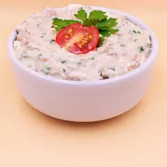 Pyszna pasta z tuńczyka i jajka, udekorowana pomidorkiem i natką pietruszki, w białej miseczce.