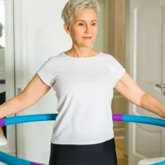 Kobieta w białej koszulce ćwiczy z kolorowym hula hop.