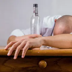 Mężczyzna śpi na biurku obok pustej butelki. Czy alkohol wypłukuje żelazo? To pytanie zadaje sobie wielu.