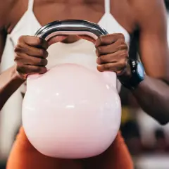 Kobieta z rozbudowanymi ramionami trzyma różową kettlebell, ćwicząc, by badz sprawny jak lampart.