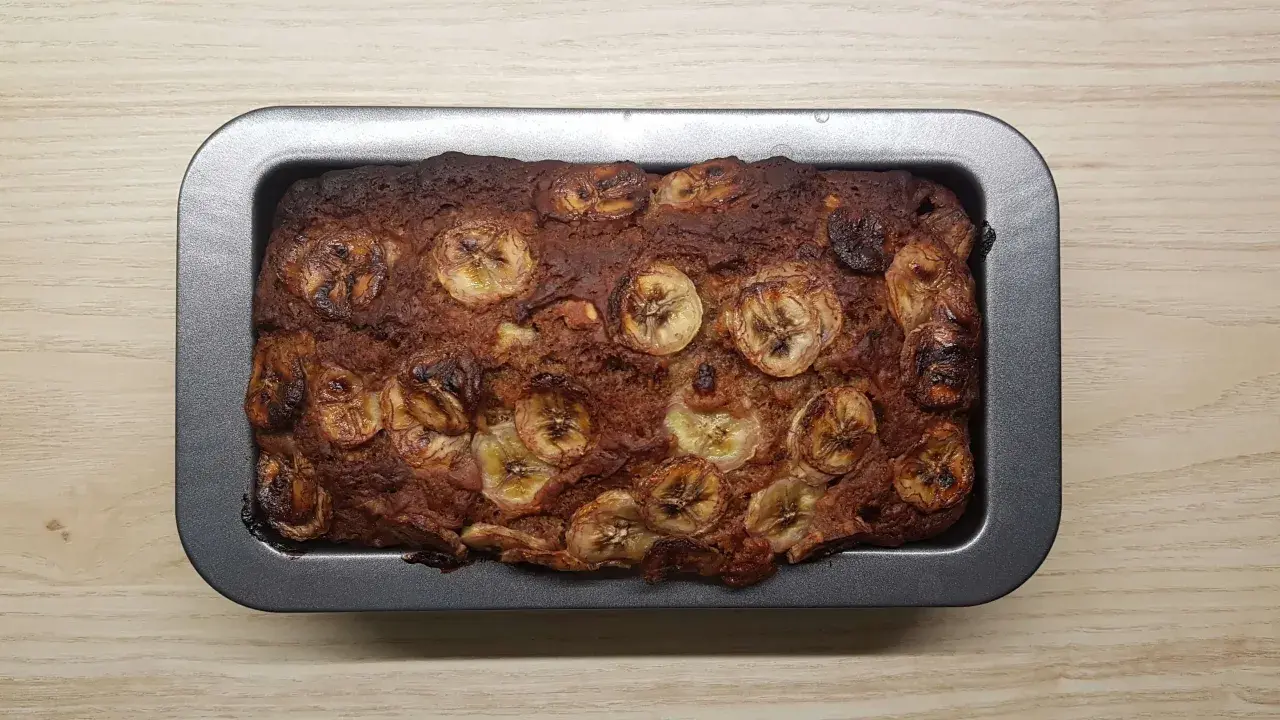 Upieczony proteinowy chlebek bananowy z plasterkami banana na wierzchu, w metalowej formie.