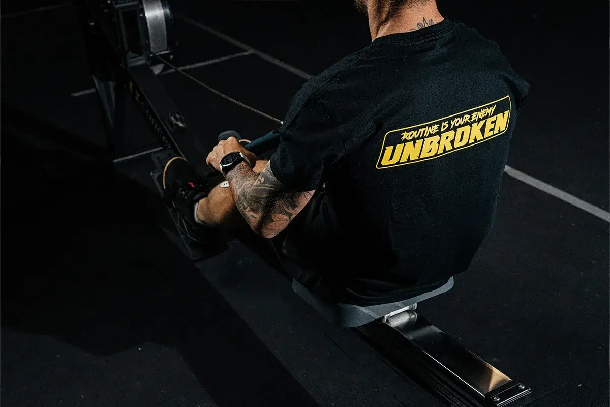 Mężczyzna z tatuażami na ramieniu trenuje na wioślarzu. Czy to crossfit czy siłownia, ważne, że jest UNBROKEN!