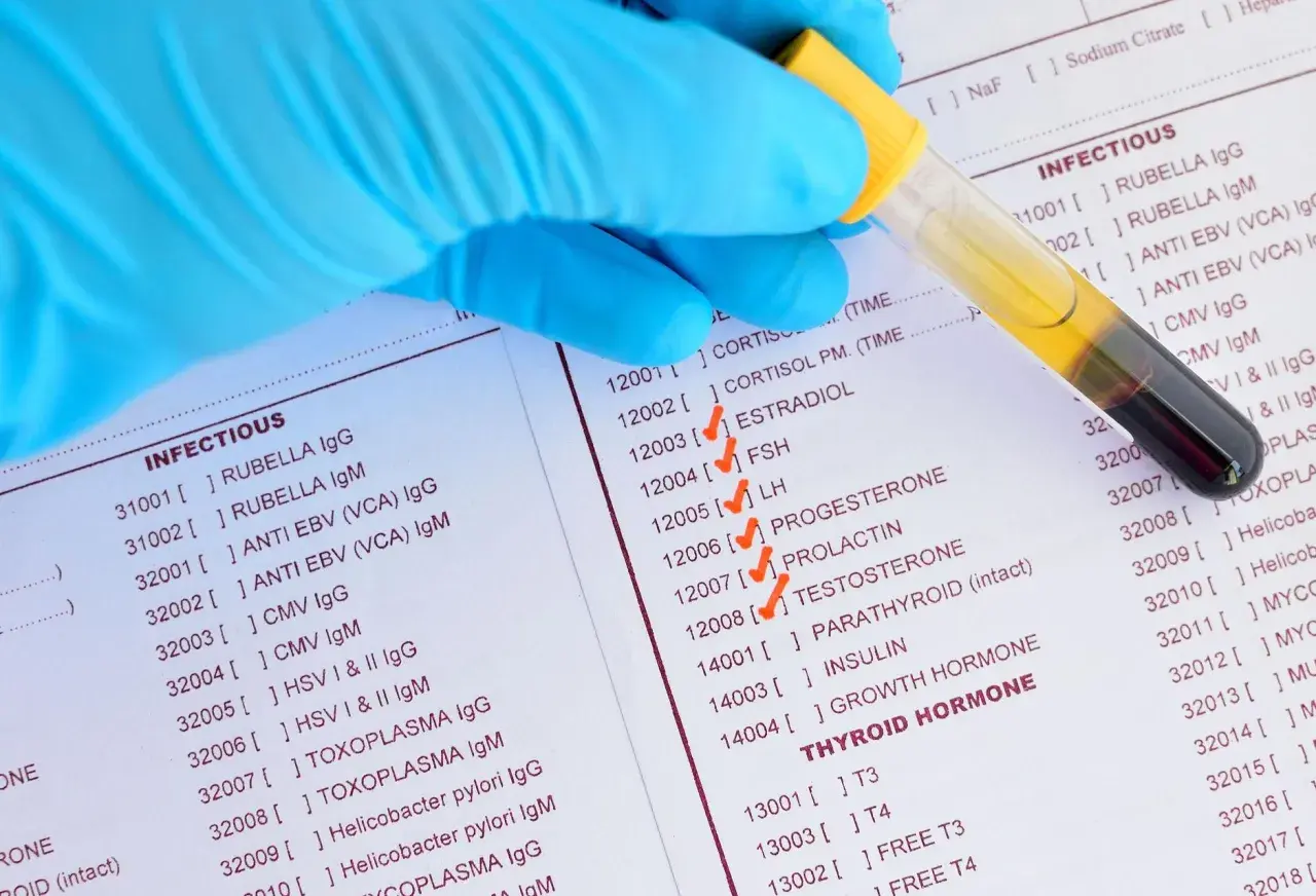 Rękawiczka pobiera próbkę krwi do badań, na liście zaznaczono estradiol.