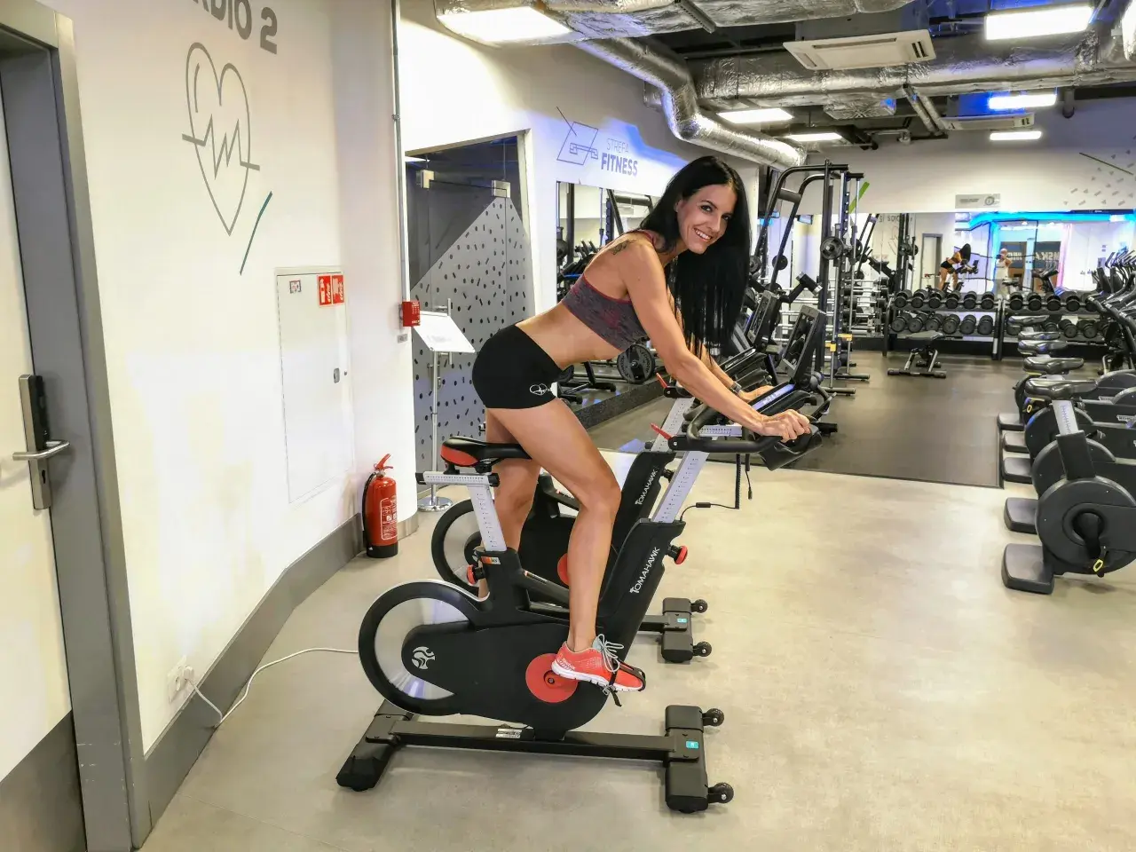 Kobieta ćwiczy na rowerze stacjonarnym w siłowni. To świetny sposób na poprawę kondycji, czy to cardio, czy kardio – ważne, by się ruszać!