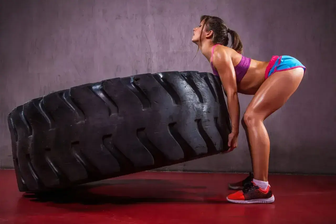 Kobieta w sportowym stroju wykonuje ćwiczenie z ogromną oponą, typowe dla treningu crossfit.