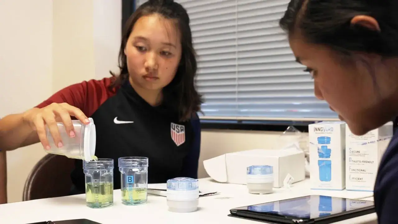 Dziewczyna w stroju sportowym USA nalewa płyn do pojemnika, przygotowując się do testu antydopingowego.
